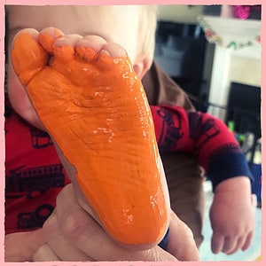 Baby's foot covered in orange paint to make Mother's Day Footprint Art