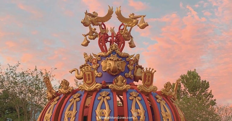 Photo of Dumbo ride at Walt Disney World with sunset in the background. Statues of storks carrying babies at top of Dumbo ride.