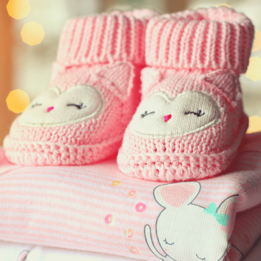 photo of pink knit owl booties on top of pink baby clothes